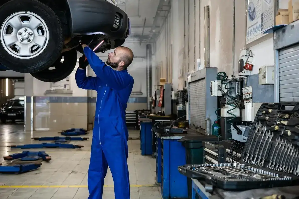 Mécanicien en bleu travaillant sous une voiture. Outils visibles, suggérant le prix de la main d'œuvre de garage.