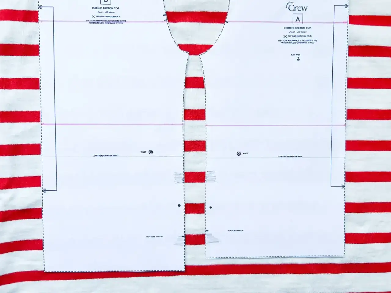 Wzór wykroju na bluzkę typu bretońskiego leży na materiale w biało-czerwone paski. Dzianina w paski idealnie pasuje do morskiego stylu.