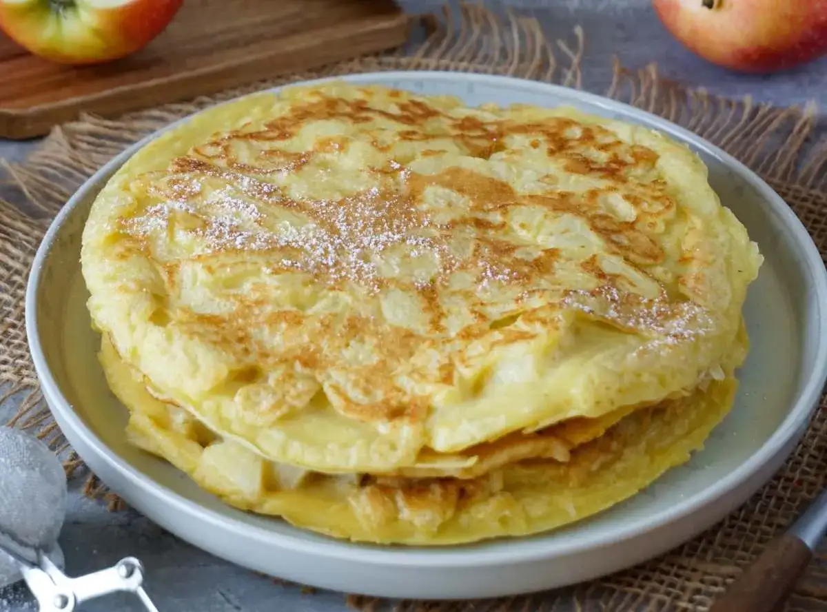 Ein gestapelter Apfelpfannkuchen, bestäubt mit Puderzucker. Ein köstliches Apfelpfannkuchen Rezept, das man ausprobieren muss!