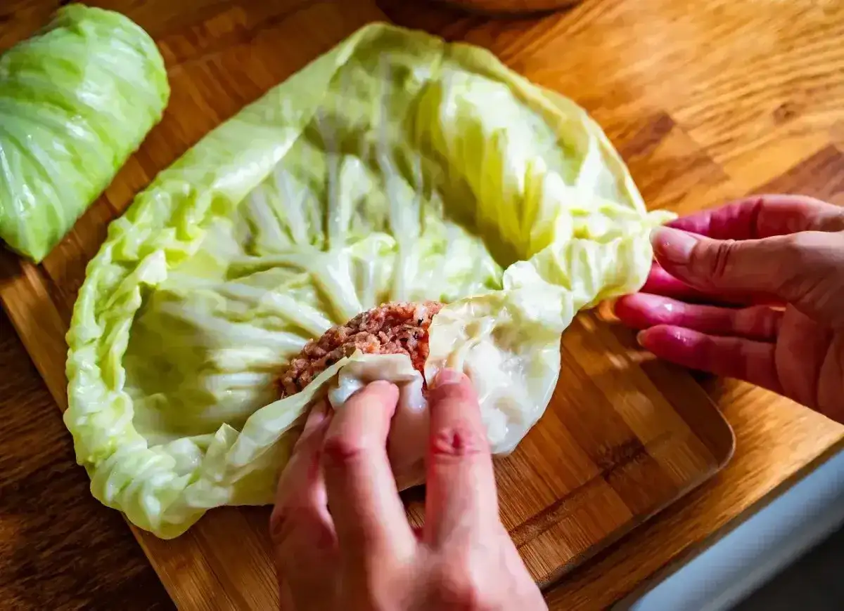 Ręce zwijają gołąbki na desce. Mięso z ryżem w liściu kapusty. Idealny przepis na gołąbki na 1kg mięsa.