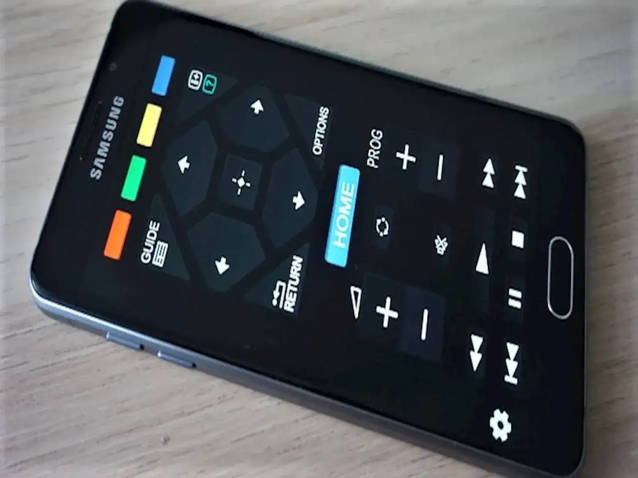 Smartfon z ekranem imitującym aplikację pilot do telewizora. Widoczne przyciski nawigacyjne, "HOME", "GUIDE", "RETURN" i inne funkcje.