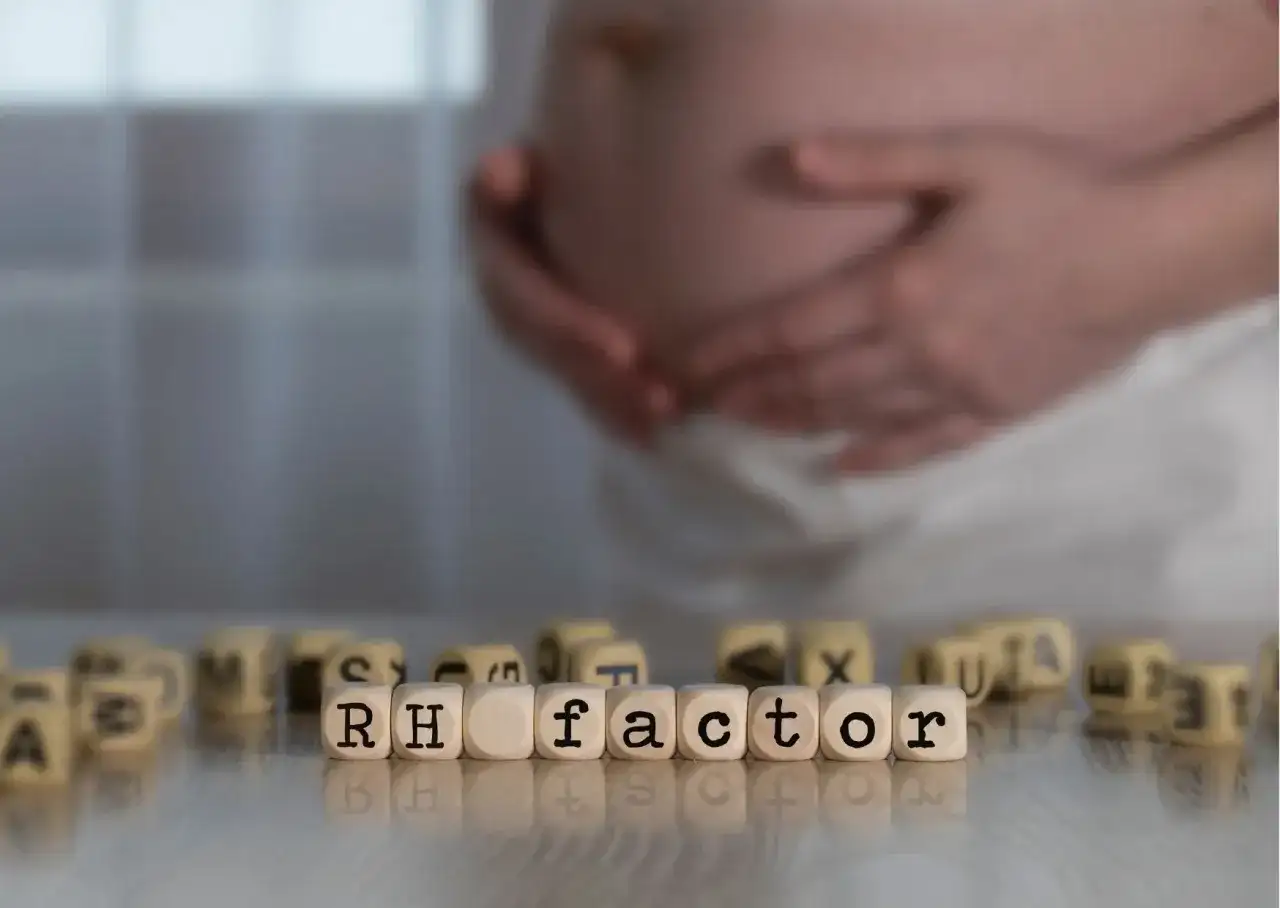 Czarne litery na kostkach układają słowo "RH factor". W tle widać brzuch kobiety w ciąży, sugerując znaczenie surowicy w tym okresie.
