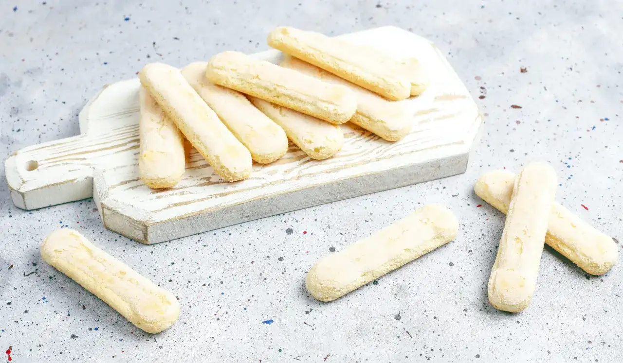 Savoiardi pronti per la ricetta del tiramisù, disposti su un tagliere bianco.