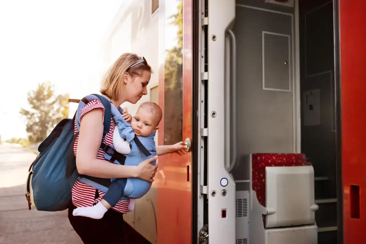 Frau mit Baby im Tragetuch steigt in den Zug. Abenteuerliches Backpacking mit Baby beginnt.