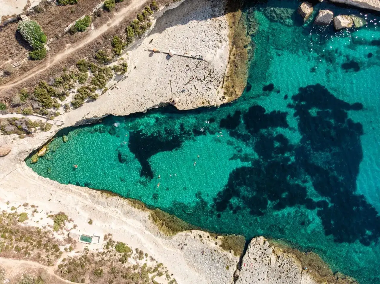Malta plaże: turkusowa woda zatoki, skaliste wybrzeże i kilka osób kąpiących się w słońcu.