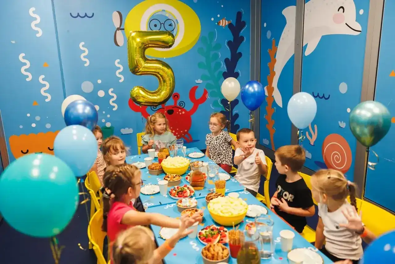 Radosna organizacja urodzin dla dzieci z motywem podwodnym. Złota piątka, balony i uśmiechnięte buzie maluchów przy stole pełnym smakołyków.