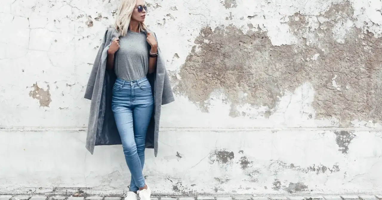 Modelka w jasnych jeansach skinny i szarym płaszczu. Dowiedz się, jakie jeansy do jakiej figury pasują najlepiej.