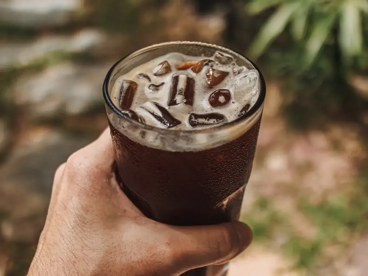 Dłoń trzyma szklankę orzeźwiającego napoju z lodem. To idealny sposób na ochłodę, gdy zastanawiasz się, cold brew co to.