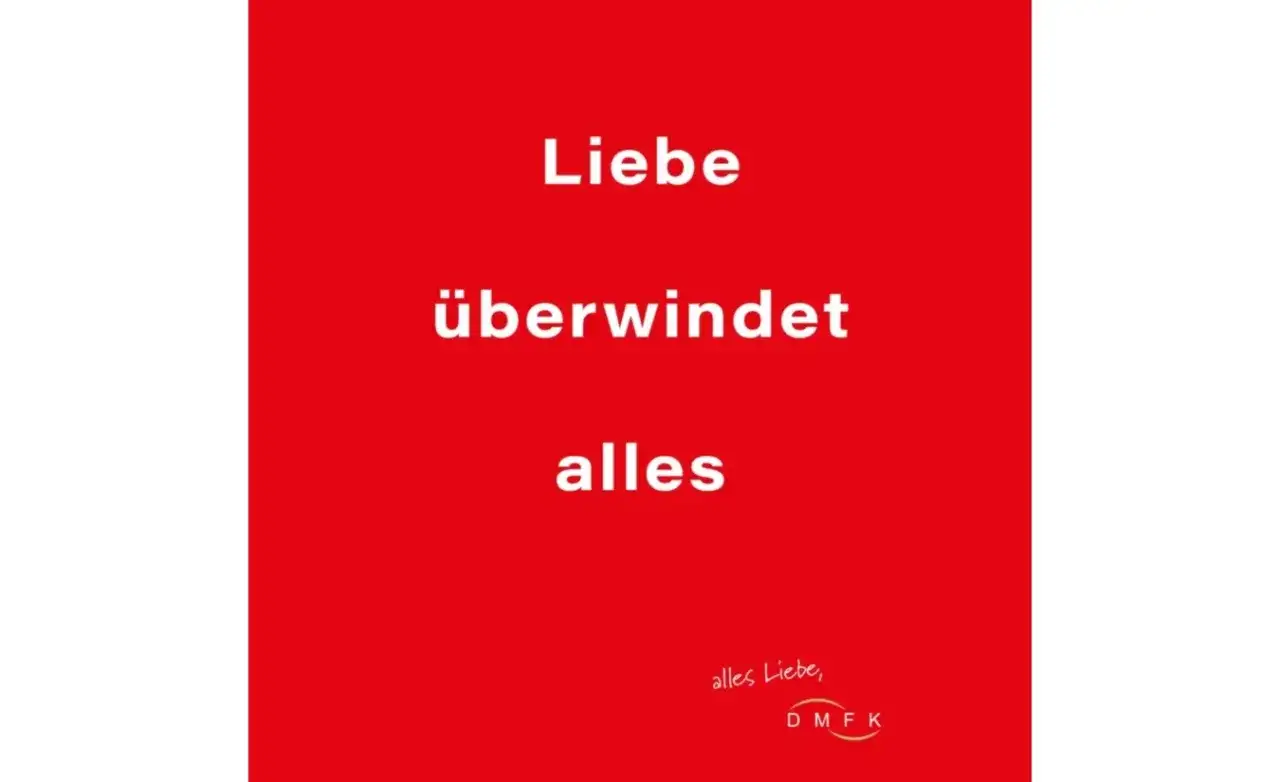 Rode achtergrond met witte tekst: "Liebe überwindet alles". Een boodschap dat liefde overwint alles, met een kleine handgeschreven tekst en logo rechtsonder.