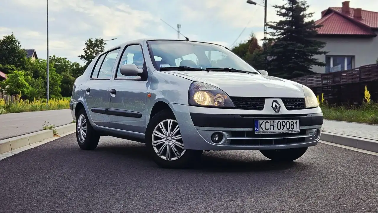 Srebrny Renault Thalia 1.4 z polskimi tablicami rejestracyjnymi KCH 09081 zaparkowany na poboczu drogi.