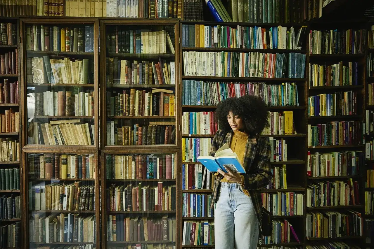 Kobieta z burzą włosów czyta książkę w bibliotece pełnej książek, jak w serii Lisy Gardner.