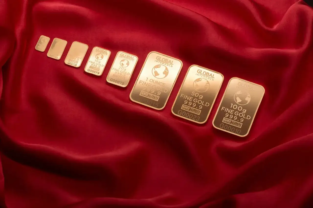 Sztabki złota Global Intergold, od najmniejszej do 100g, ułożone na czerwonym jedwabiu. Wśród nich widać combibar Valcambi.
