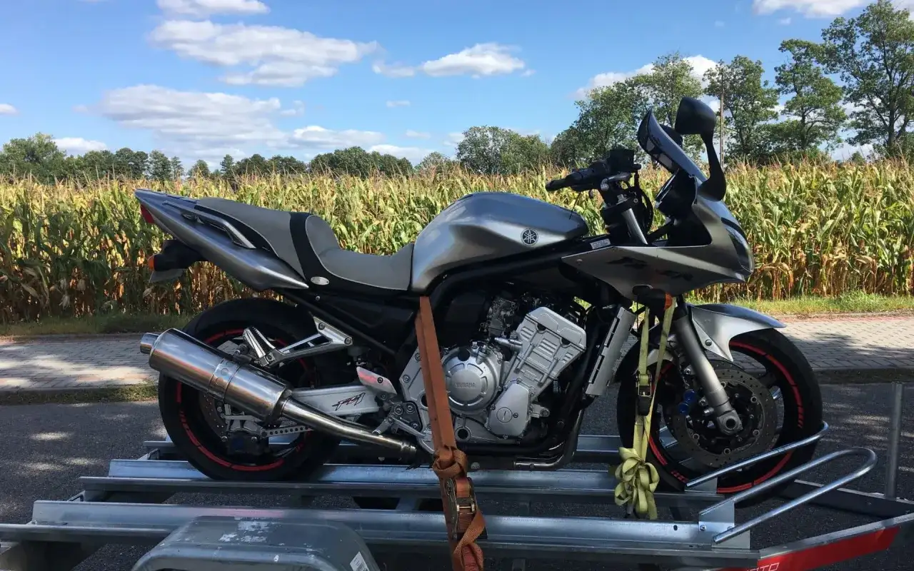 Srebrny motocykl Yamaha Fazer na przyczepce, gotowy do przerejestrowania. W tle pole kukurydzy i błękitne niebo.