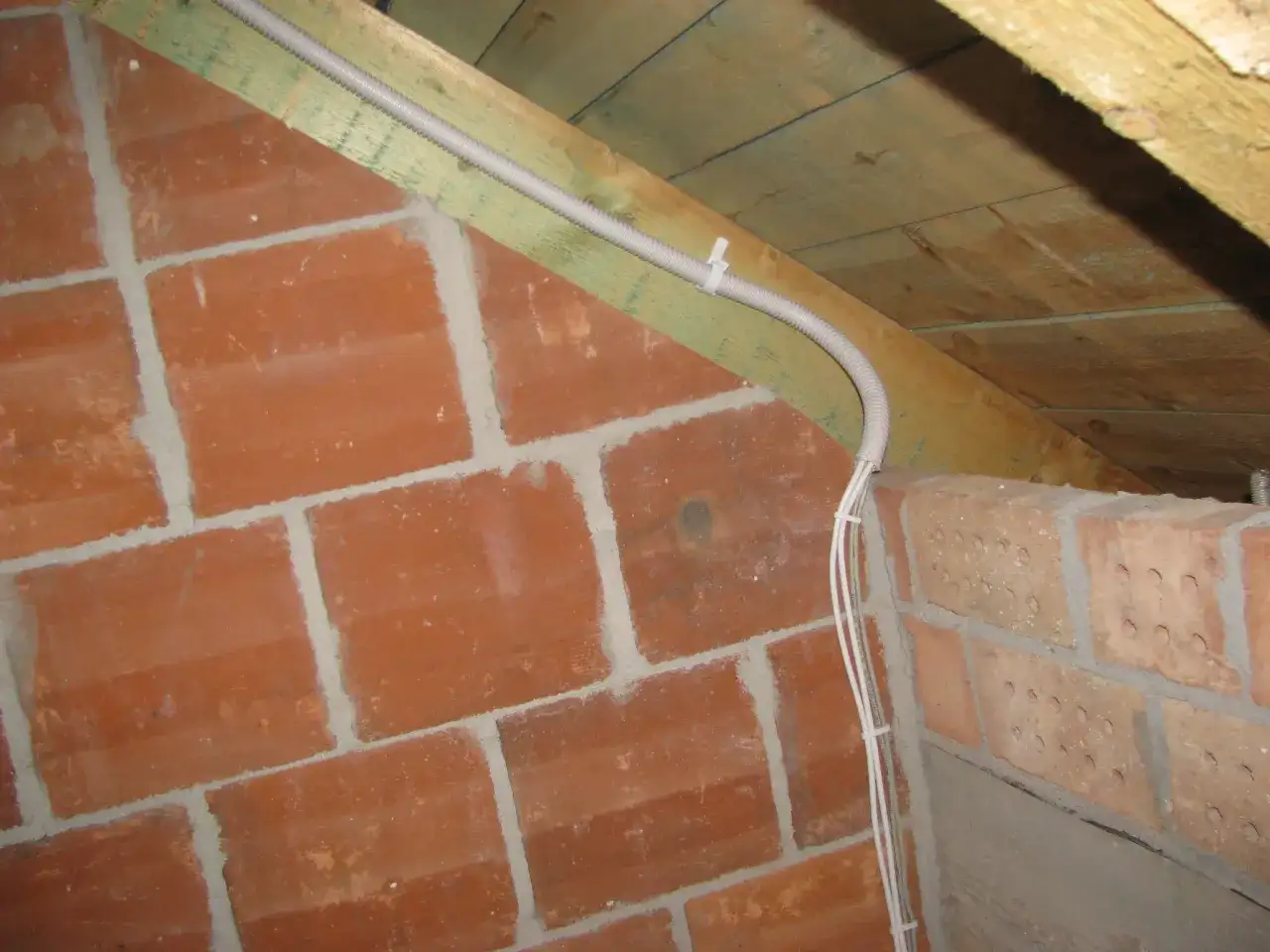 Instalacja elektryczna w peszlu na poddaszu, obok ceglanej ściany. Czy przewody elektryczne muszą być w peszlu? Tak, dla bezpieczeństwa.