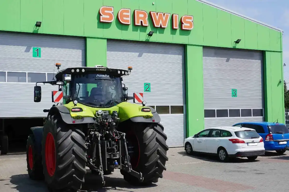 Traktor przed zielonym budynkiem serwisu. Zastanawiasz się, ile kosztuje roboczogodzina mechanika?