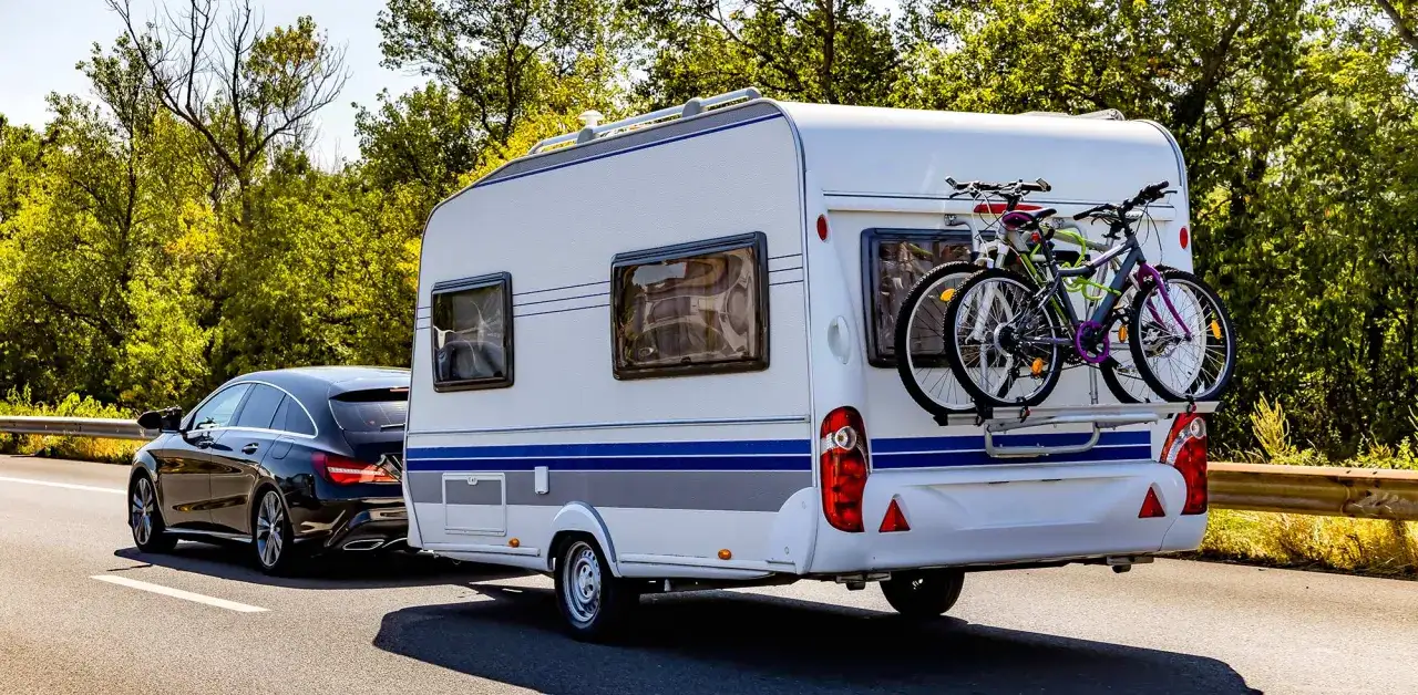 Schwarzer Kombi zieht Wohnwagen mit Fahrrädern, bereit für den Urlaub. B96 oder BE, das ist hier die Frage für die Reise.