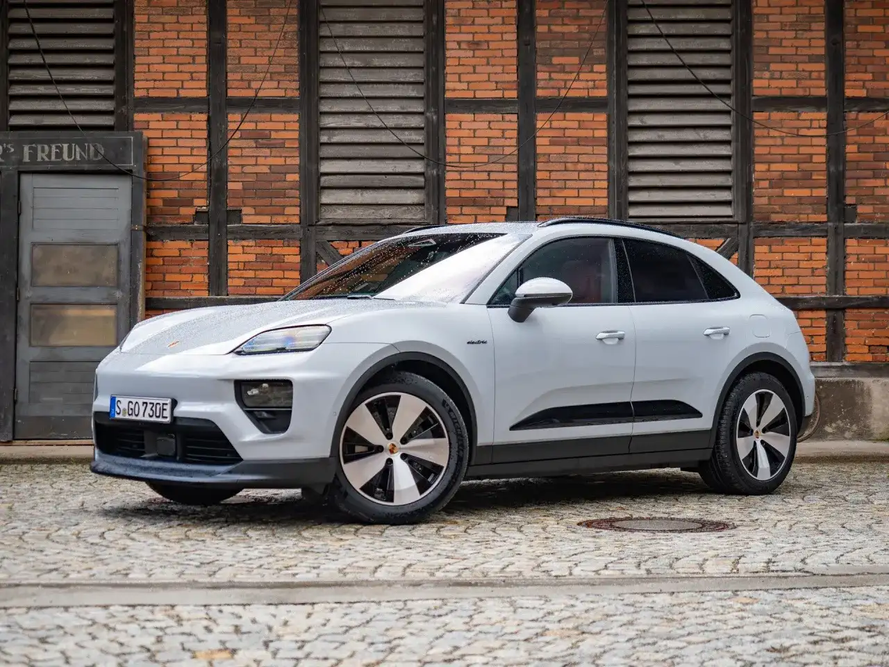 Biały Porsche Macan Electric na bruku przed ceglanym budynkiem. Sprawdź aktualną porsche macan cena.