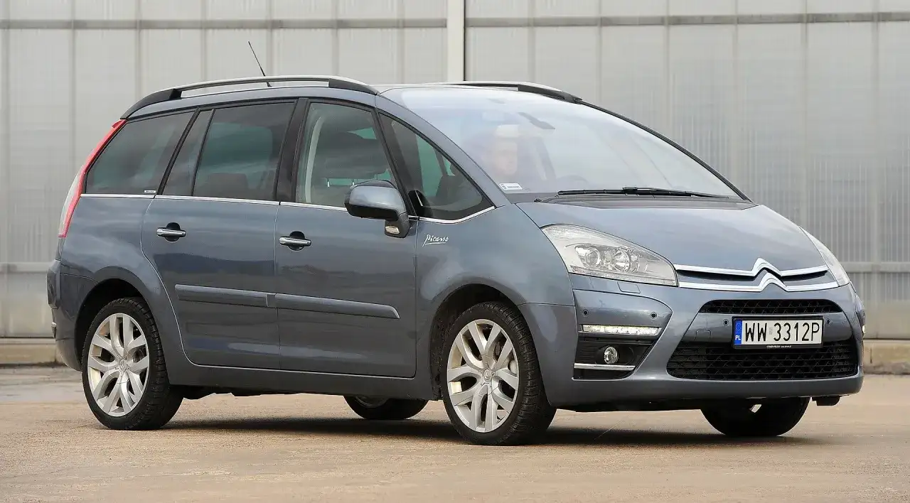 Szary Citroen C4 Grand Picasso 2.0 HDI z kierowcą za kierownicą, zaparkowany przed budynkiem.