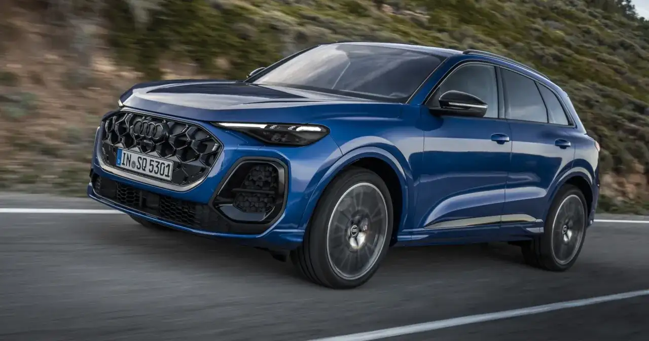 Niebieskie, nowe Audi Q5 z charakterystycznym grillem i ostrymi światłami pędzi po krętej drodze wśród wzgórz.