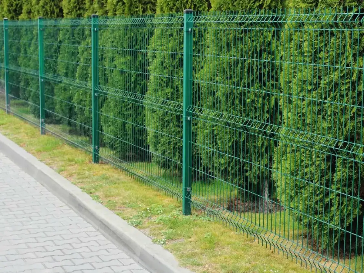 Solidne elementy ogrodzeniowe panelowe w zielonym kolorze, tworzące estetyczną barierę przed gęstym żywopłotem.