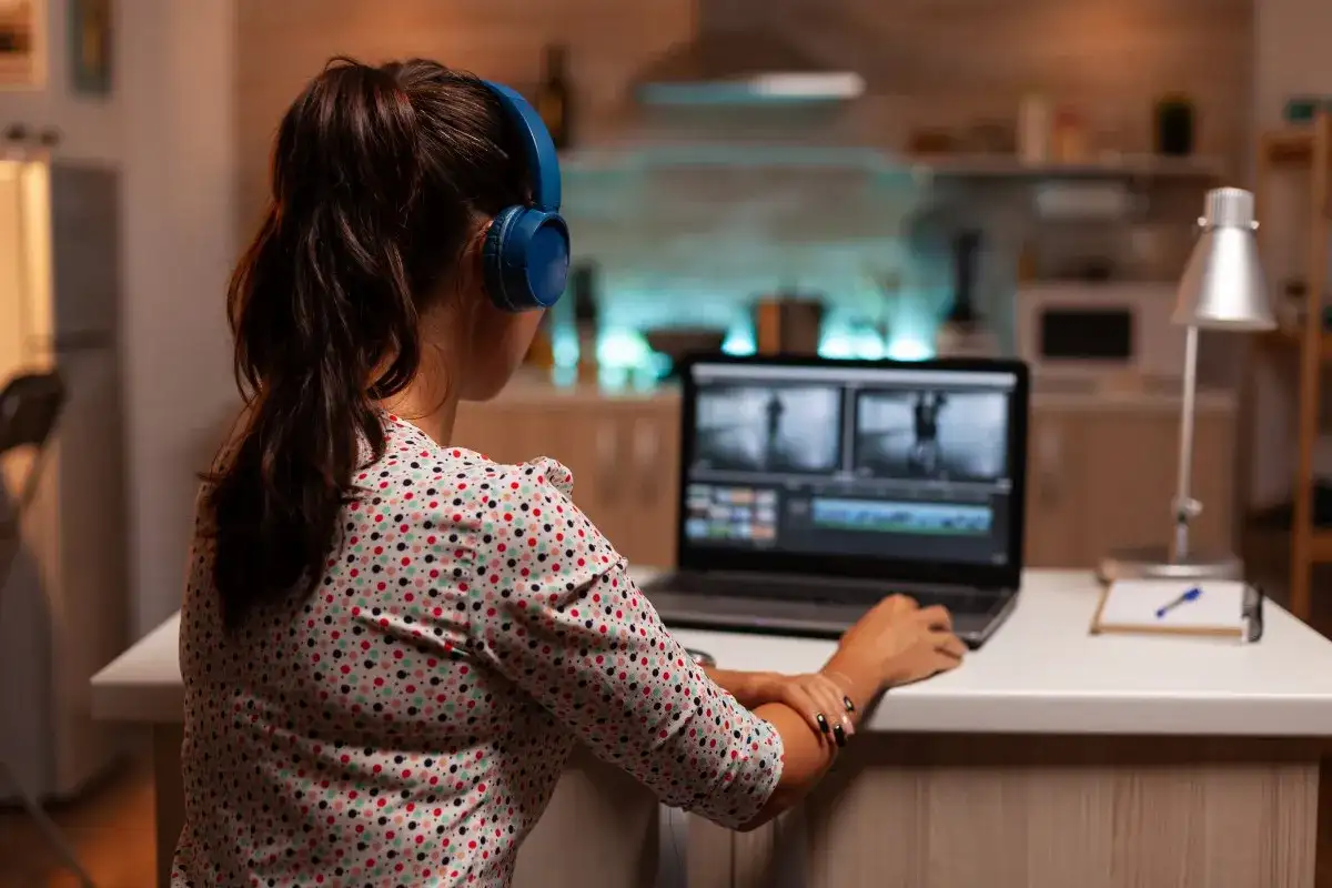 Kobieta w słuchawkach pracuje na laptopie, edytując film. Uczy się, jak zmniejszyć rozmiar filmu, by był łatwiejszy do udostępnienia.
