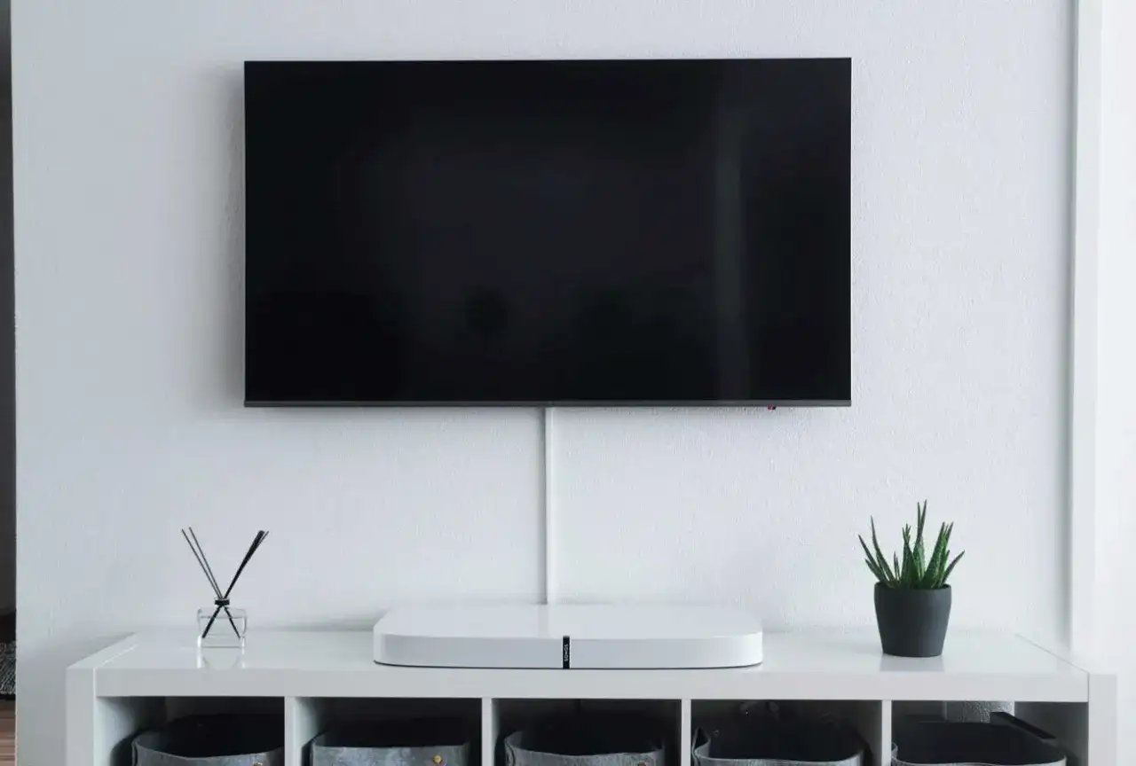 Minimalistyczny salon z telewizorem zamontowanym na ścianie. Pod nim biała szafka z ozdobami i schowkami. Idealna na jakiej wysokości telewizor.