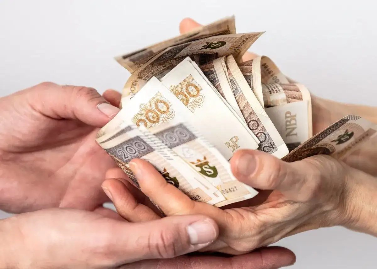 Dwie pary rąk przekazują sobie plik banknotów 200 zł. Może to być darowizna, od której należy zapłacić podatek od darowizny.