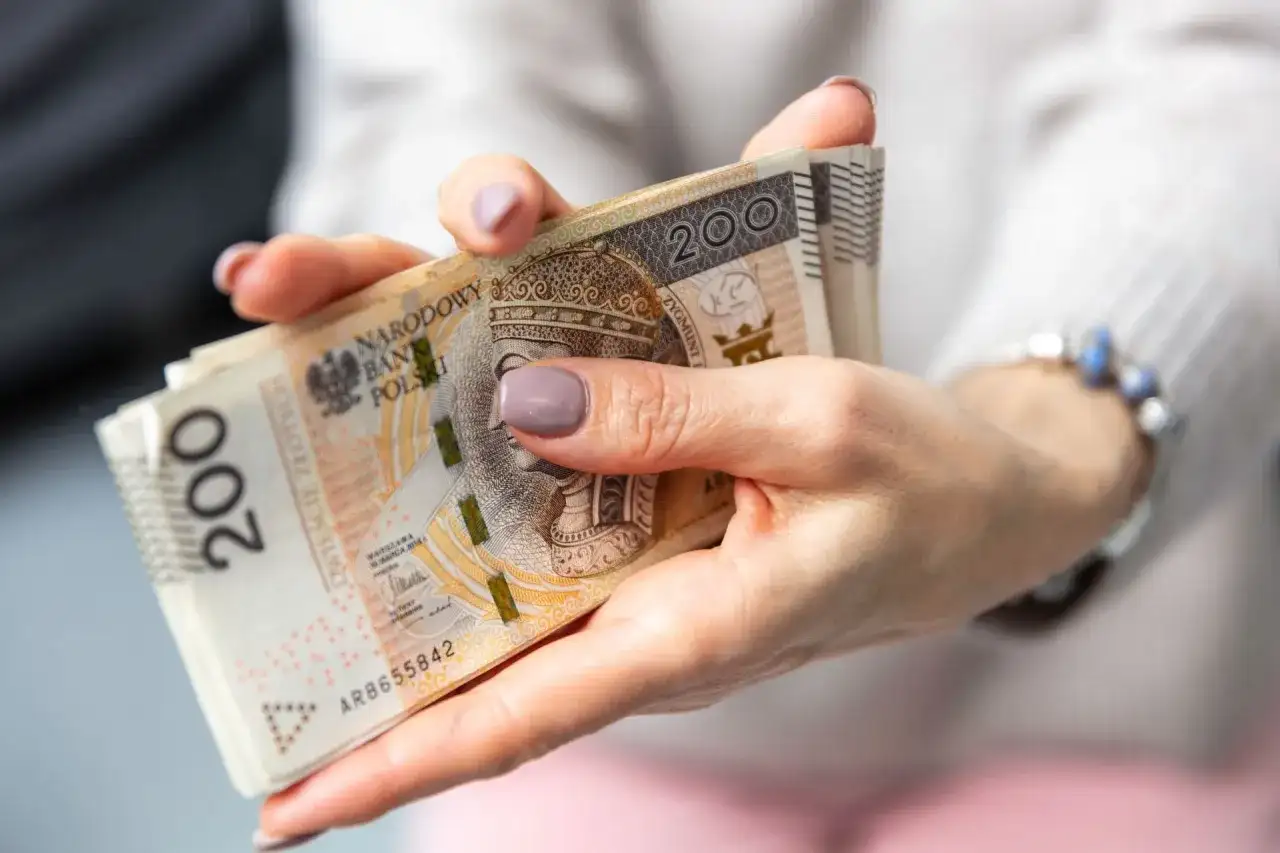 Dłonie trzymające stos banknotów 200 zł. Zastanawiasz się, jak wypłacić pieniądze z PPK?