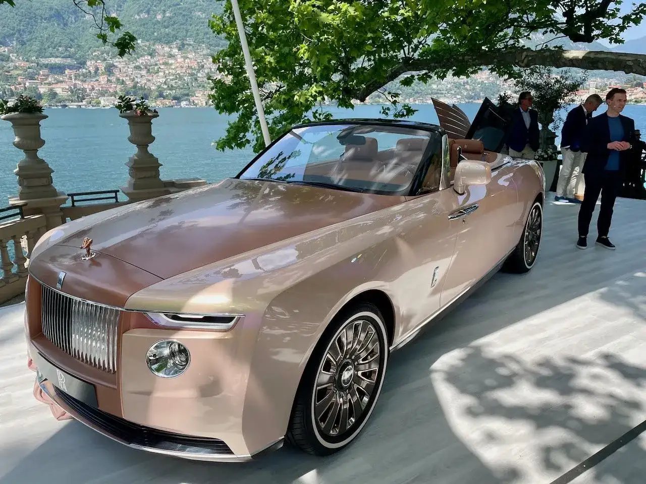 Elegancki Rolls-Royce Boat Tail w kolorze szampańskim, prezentowany nad jeziorem Como, przyciąga wzrok swoim unikalnym designem.