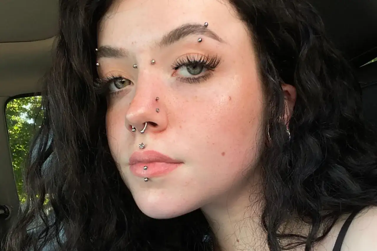 Młoda kobieta z wieloma kolczykami, w tym kolczyk w brwi, septum i wargach.