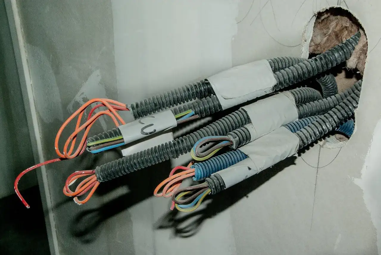 Przewody elektryczne w peszlach wychodzące ze ściany. Widać kolorowe żyły, gotowe do połączenia. To etap prac, jak przedłużyć przewód elektryczny w ścianie.