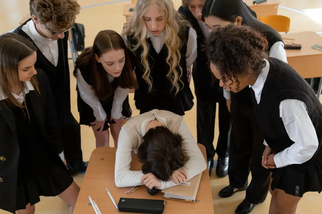 Uczniowie patrzą na skuloną koleżankę przy ławce. Scena pokazuje, czym jest bullying.