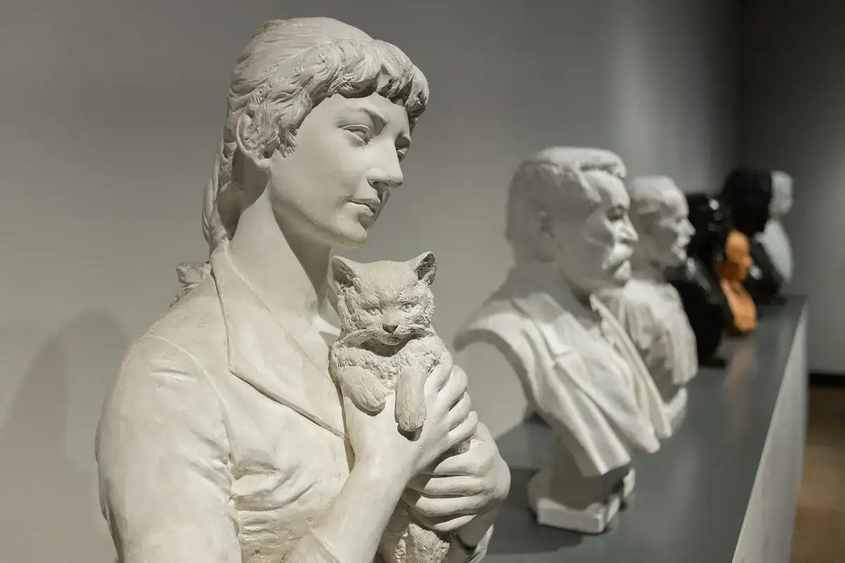 Rzeźba Camille Claudel "Plotkarki" - kobieta z kotem, obok popiersia mężczyzn.