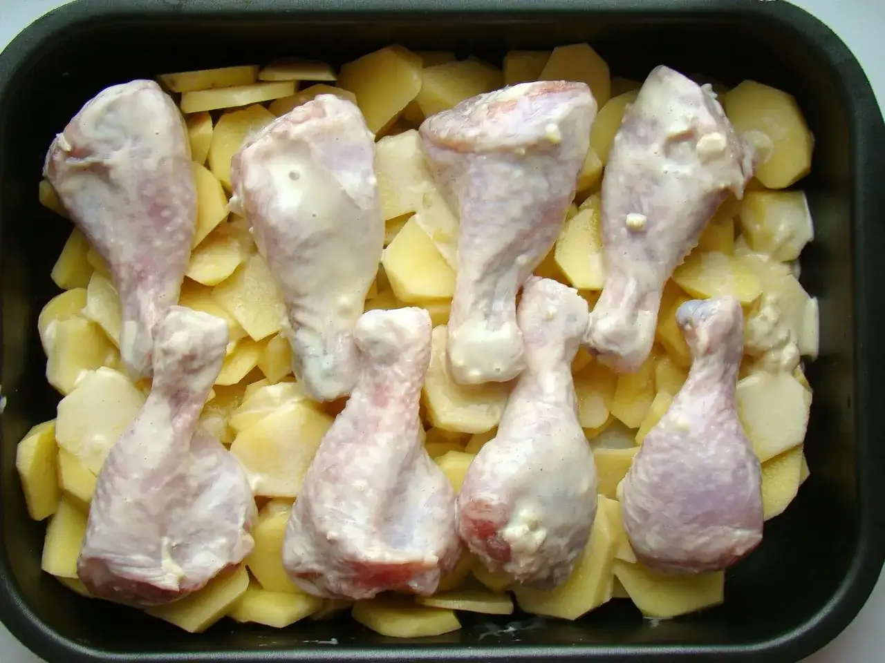 Pałki kurczaka w sosie, ułożone na ziemniakach w naczyniu żaroodpornym. Idealne do pieczenia, by uzyskać chrupiące danie.