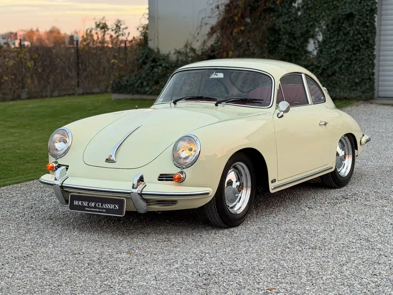 Klasyczny kremowy Porsche 356 z czerwoną tapicerką, zaparkowany na żwirowej nawierzchni.