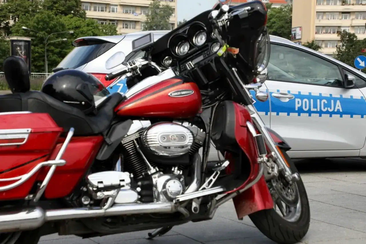 Czerwony motocykl Harley-Davidson obok radiowozu. Czyżby ktoś próbował jeździć bez prawa jazdy?