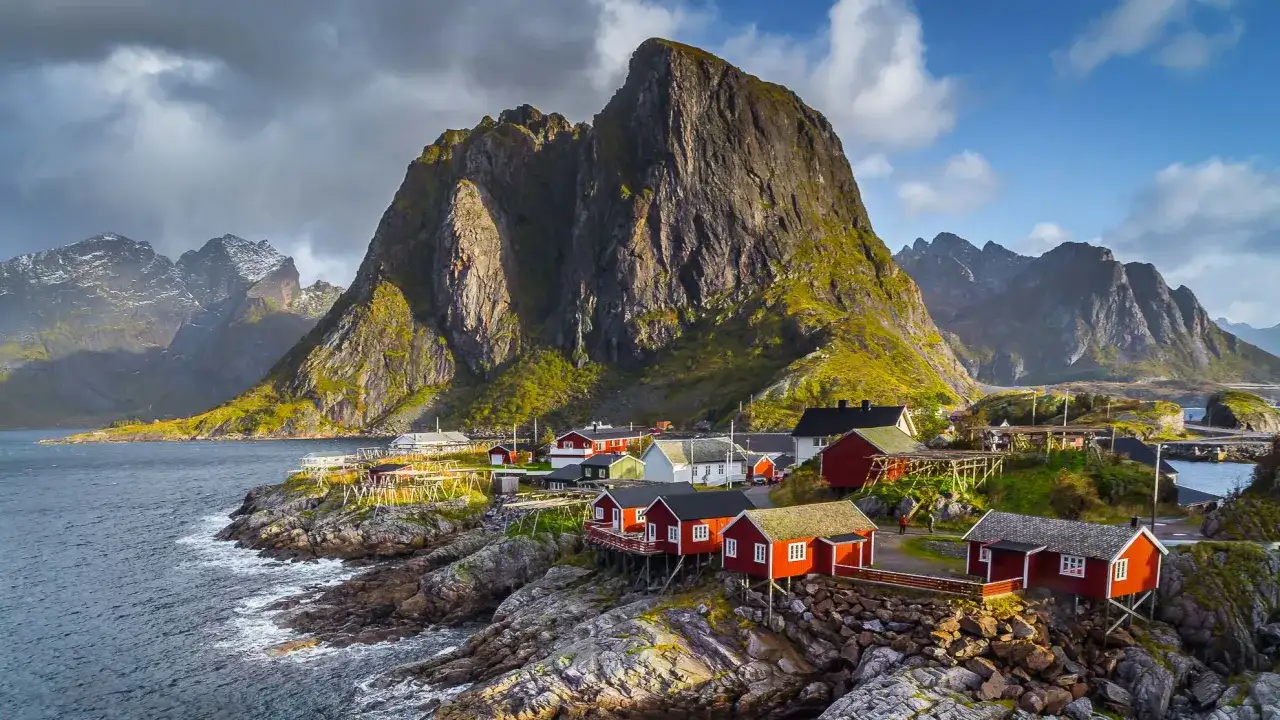 Traumhafte norwegen route 2 wochen: Rote Fischerhäuser am Fuße steiler Berge an der Küste.