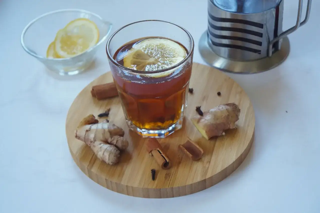 Szklanka aromatycznej herbaty z cytryną, obok świeży imbir do herbaty, laski cynamonu i goździki. Idealne na chłodne dni.