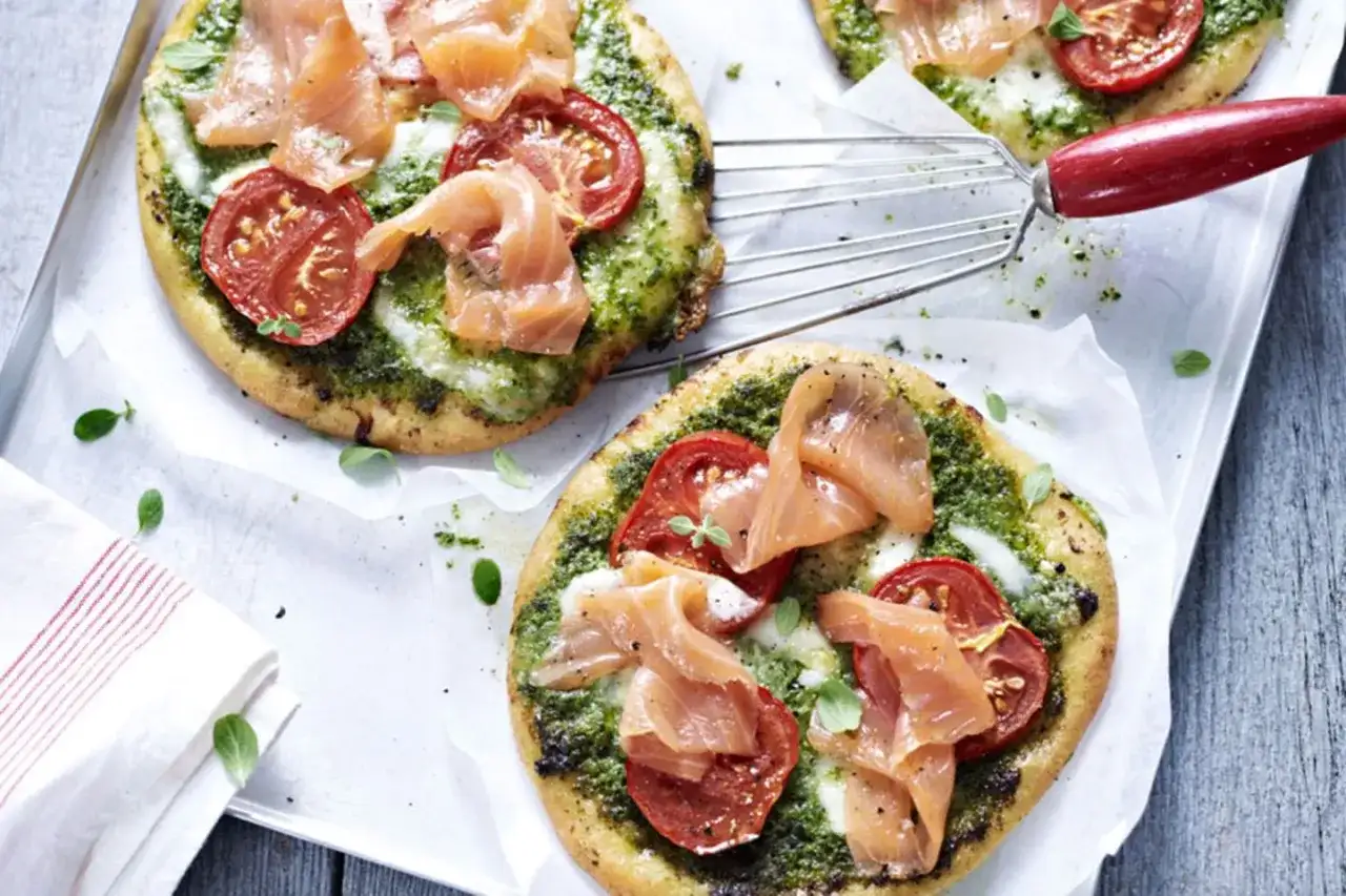 Zwei kleine Pizzen mit Pesto, Tomaten und Lachs auf einem Blech.
