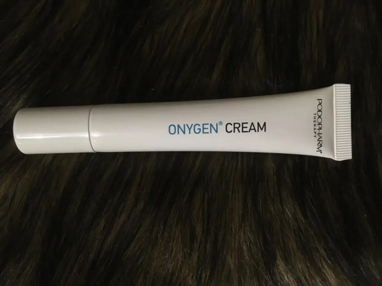 Biała tubka kremu OXYGEN CREAM na ciemnym, futrzanym tle.