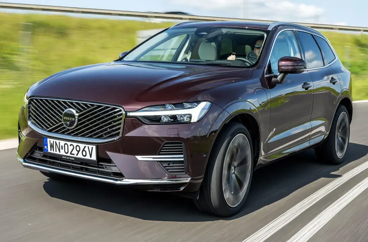 Elegancki, bordowy Volvo XC60 T5 w ruchu drogowym. Kierowca w okularach prowadzi SUV-a po asfaltowej drodze, otoczonej zielenią.
