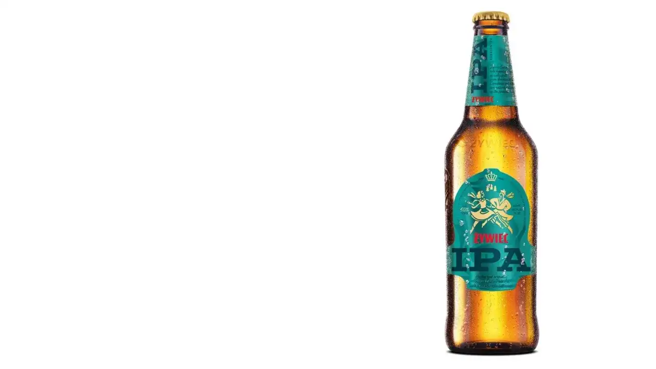Chłodne piwo Żywiec IPA z kroplami rosy na butelce. Etykieta w kolorze turkusowym z tańczącymi postaciami i koroną.