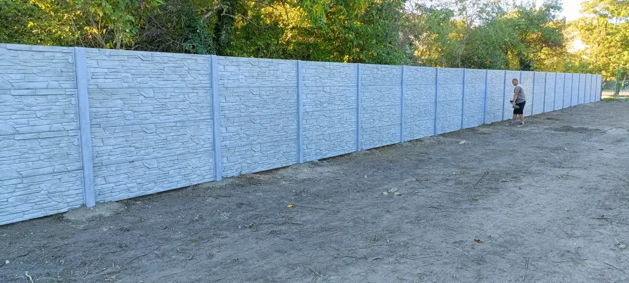 Mężczyzna z łopatą przy betonowym ogrodzeniu, zastanawia się, jak podwyższyć ogrodzenie betonowe, by zyskać więcej prywatności.