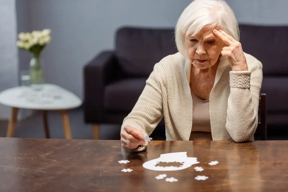 Starsza kobieta zmagająca się z układanką, symbolizującą wczesny alzheimer. Jej zamyślona twarz i gest wskazują na trudności z pamięcią.