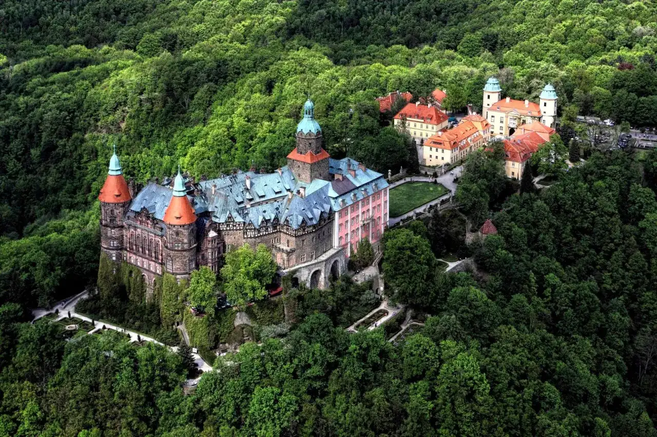 Zamek **Chudów** otoczony bujną zielenią, z charakterystycznymi wieżami i czerwonymi dachami, wygląda jak z bajki.
