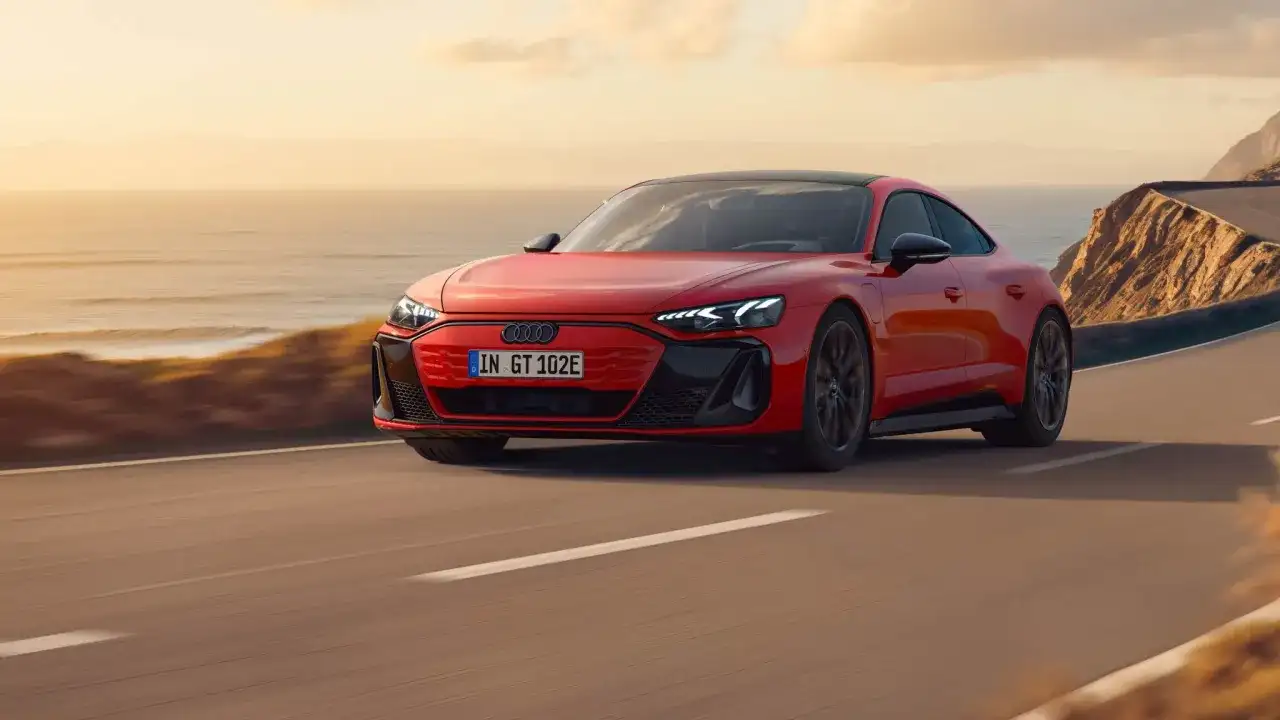 Czerwony Audi e-tron GT sunie po malowniczej nadmorskiej drodze o zachodzie słońca.