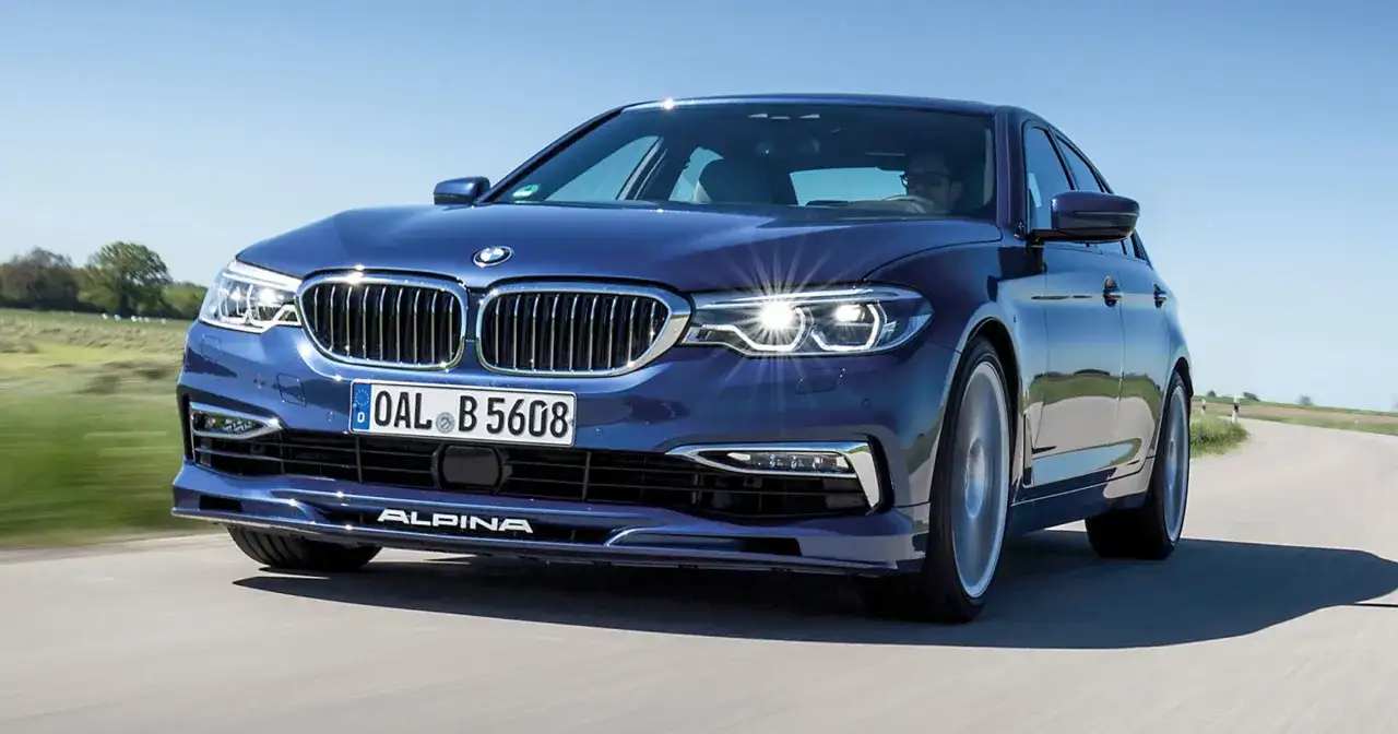 Niebieskie BMW Alpina pędzi po krętej drodze, błyszcząc w słońcu.