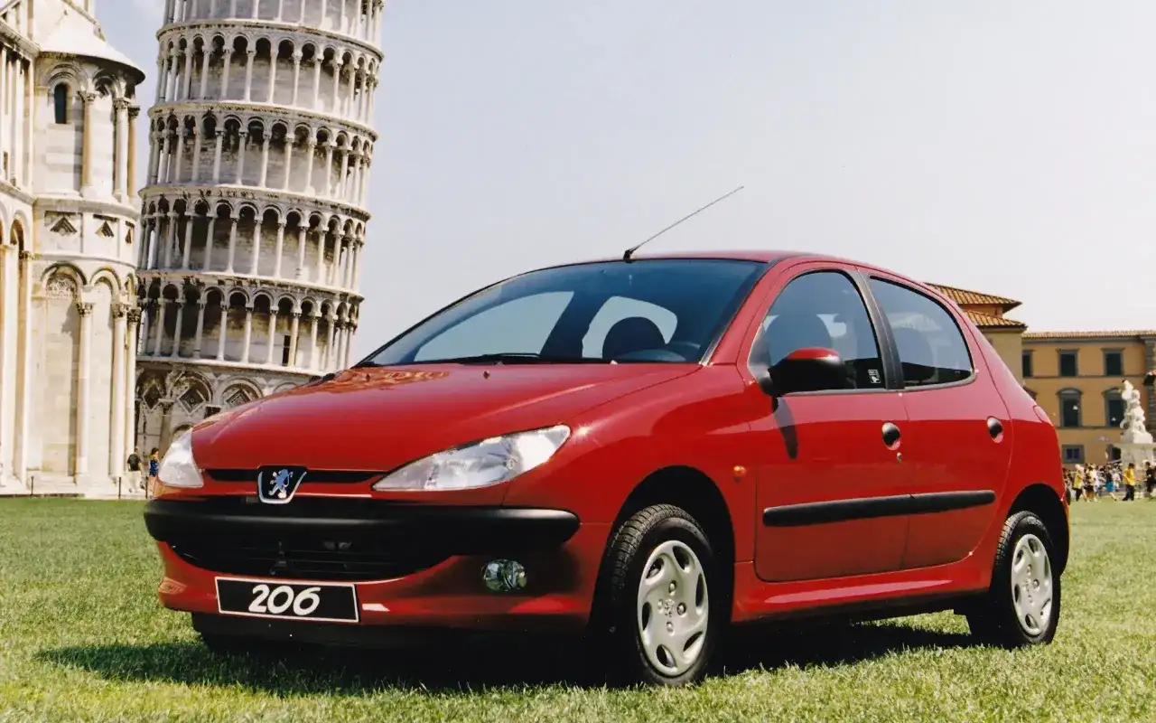 Czerwony Peugeot 206 na tle Krzywej Wieży w Pizie.