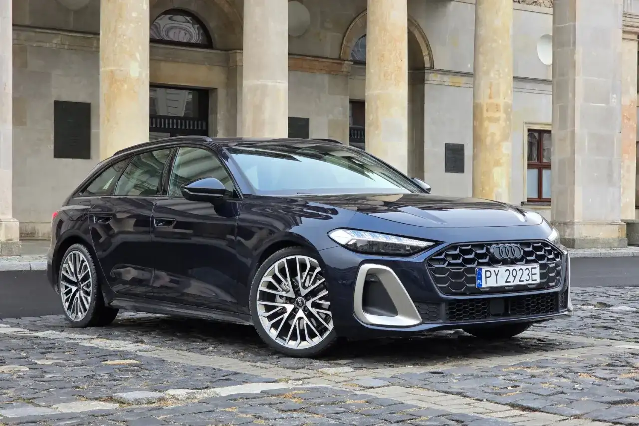 Elegancki, ciemnogranatowy Audi A5 Avant 2025 z charakterystycznym grillem i felgami stoi przed zabytkową budowlą.
