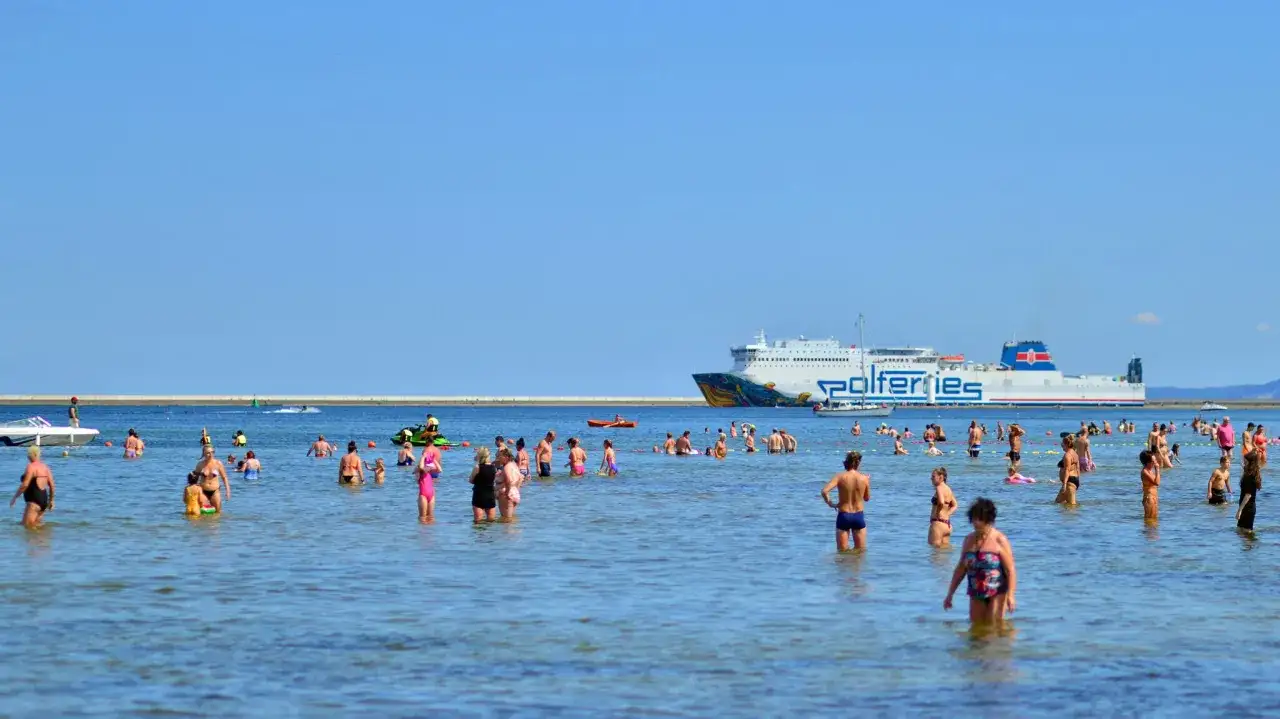 Ludzie kąpią się w morzu, a w tle płynie prom do Ystad.